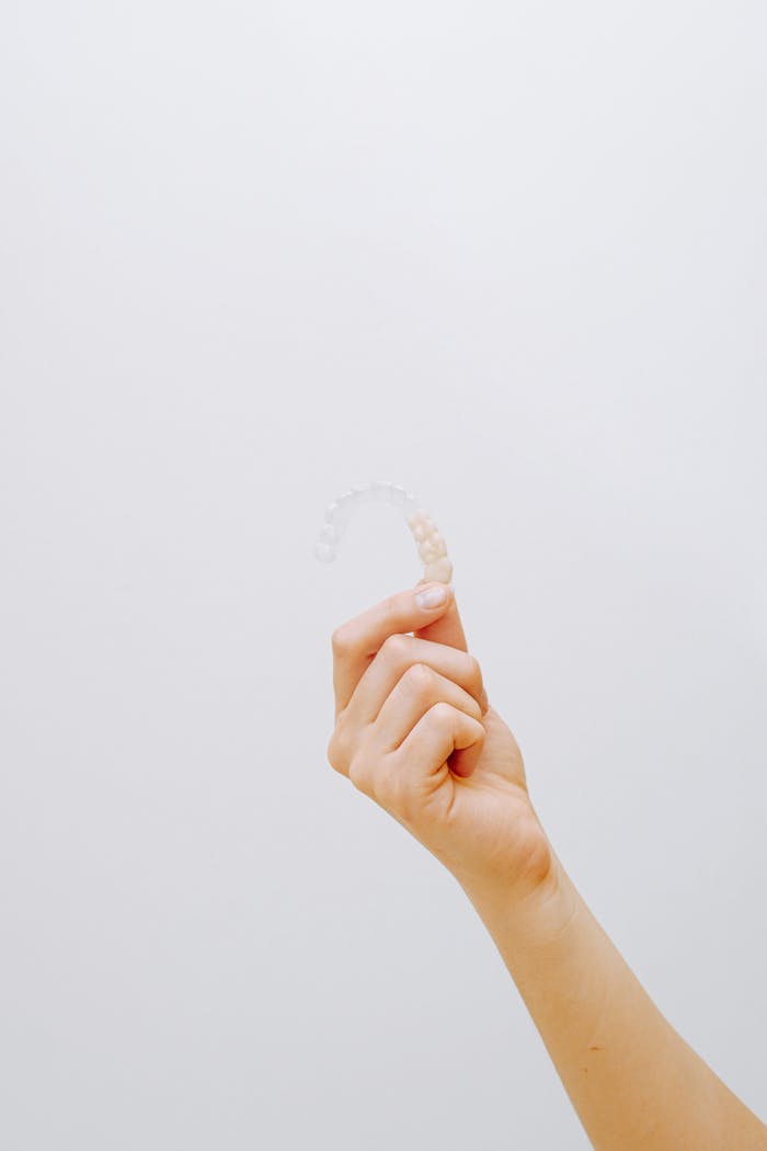 Services Close-up of a hand holding a clear dental aligner against a white background, emphasizing orthodontic care.